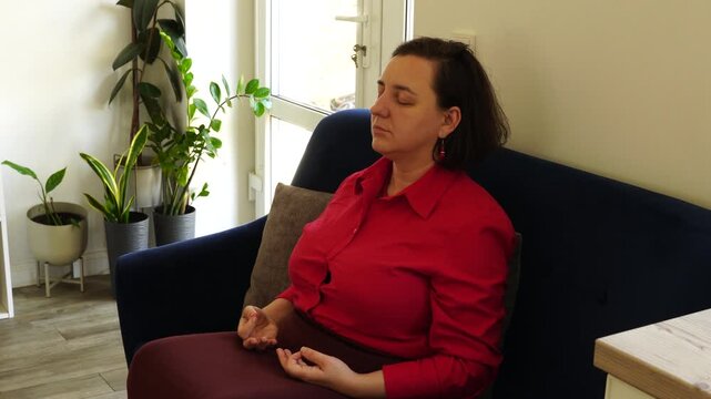 Woman sits on the sofa and meditates during working day at the office
