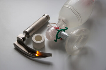 A laryngoscope, adhesive plaster and an Ambu breathing bag are on a white table. Horizontal shot.