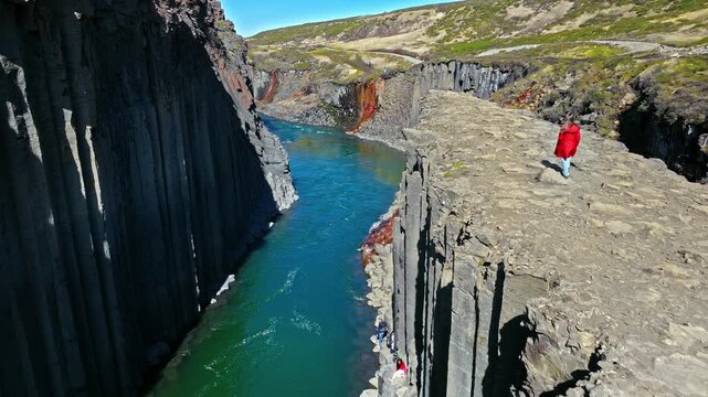 Tourist exploring Stu&eth;lagil Canyon in East Iceland. Woman walking along narrow basalt ledges overlooking the turquoise river gorge.