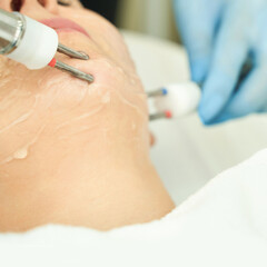 Naklejka premium Female receiving facial treatment with skincare device at spa clinic for rejuvenation and relaxation.