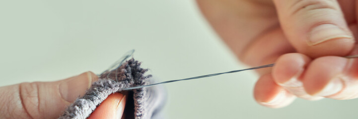 Close-up of caucasian female hands sewing with needle and thread on fabric.