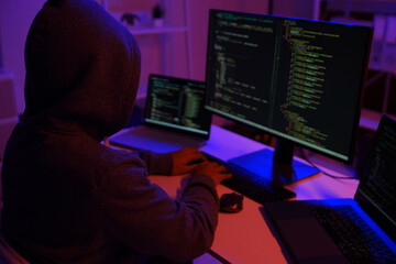 A mysterious hooded hacker working on a computer in a dark room.