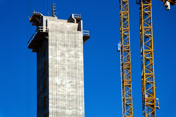 Two yellow cranes on skyscraper construction site of timber building Kaj 16 with hybrid concrete frames, sunny day, Lilla Bommen area, Gothenburg, Sweden