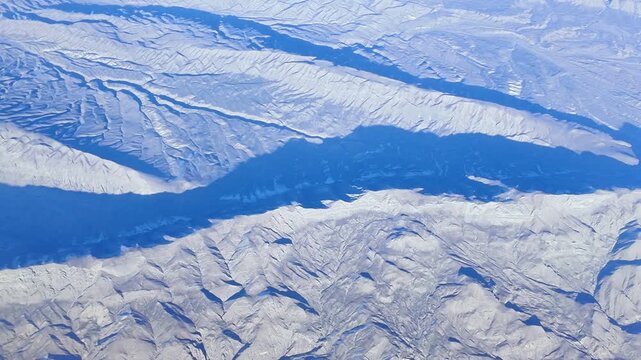 Captivating aerial shot of towering mountains, revealing stunning contrasts between peaks and shadows amid peaceful winter serenity, motion