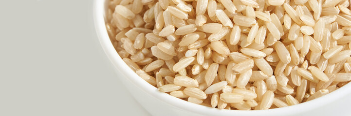 Close-up of organic brown rice grains in white ceramic bowl on light background.