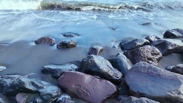 view of Ubud coastline featuring jet black volcanic stones embraced by foamy waves, embodying beauty and intensity of tropical paradise