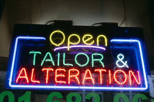 Bright neon sign indicating a tailor and alteration shop open for business in the city at night