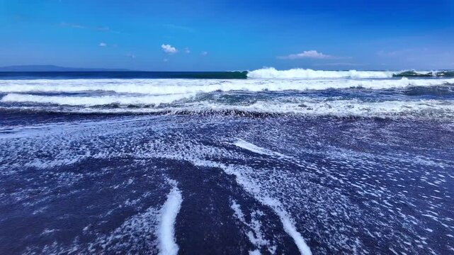 Dynamic coastal scene at Ubud with dark volcanic sand standing resilient against ocean waves that crash passionately, capturing Bali enchanting spirit