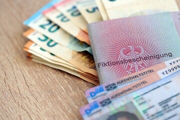 German Permanent resident card and document specimen with euro money bills lies on wooden table close up. Aufenthaltstitel and Fiktionsbescheinigung