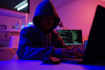 A mysterious hooded hacker working on a computer in a dark room.