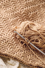 Crochet hooks and balls of beige yarn on textured crochet background. Crochet supplies.