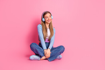 Charming girl with headphones sitting on a pink background enjoying music and relaxation in casual trendy attire