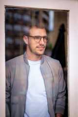 Portrait of a young man standing by the window and deep in thought