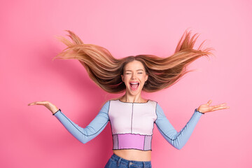 Joyful young woman tossing her hair, laughing with happiness against a vibrant pink background,...