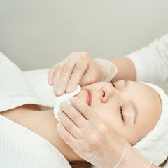 Young caucasian female receiving facial treatment at spa with professional beautician in white gloves.