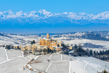 A medieval village on the hill and snow-covered vineyards against backdrop of the snow-capped Italian Alps.