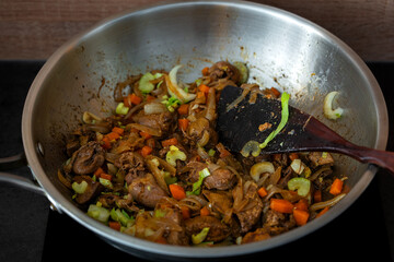 Preparing a warm chicken liver and celery salad at home, the ingredients in a steel skillet with olive oil and seasonings