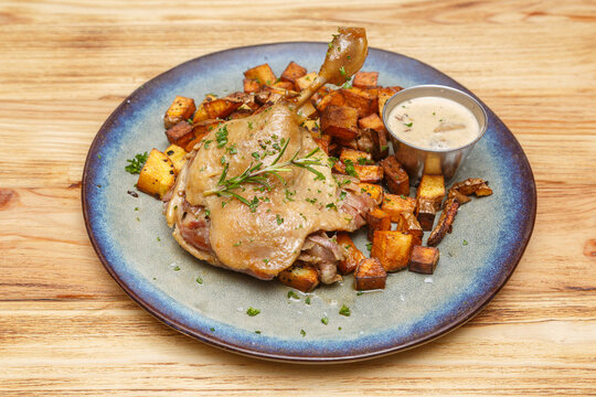 Confit de canard &ndash; plat bistro fran&ccedil;ais servi avec pommes de terre saut&eacute;es et sauce foresti&egrave;re sur une table en bois.