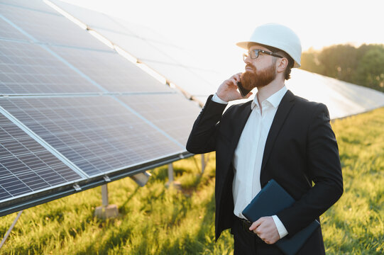 Investor wearing white hardhat using smartphone near solar panels
