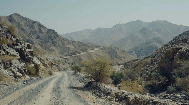 View from a vehicle on a winding, dusty road through arid mountain terrain under a hazy sky - Powered by Adobe