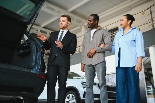 Car salesman showing trunk to african american couple in dealership