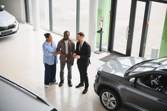Car salesman showing new vehicle to african american couple in dealership