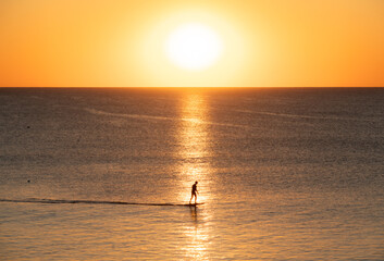 Fototapeta premium A serene silhouette of a paddleboarder glides across calm ocean waters during a golden Florida sunrise at South Ponte Vedra Beach