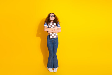 Young female student stands against a bright yellow background smiling while holding a checkerboard notebook showcasing casual fashion and playful energy