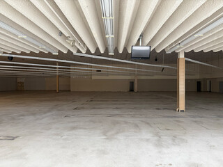 Vacant empty supermarket, retail store interior with exposed ceiling lights, blank walls, and wide open concrete floor space
