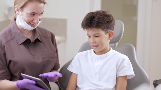 Child boy watches cartoons on computer tablet in hands of dentist at dental clinic.