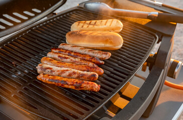 Grilling sausages and buns in a backyard barbecue during sunset