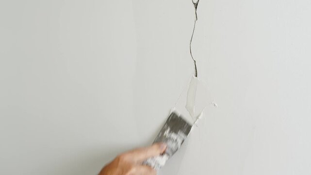A plasterer's hand repairs a wall by applying putty with a spatula, concept of timely repair and maintenance of houses and apartments