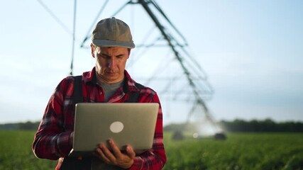 Inspecting crop with laptop in field while farmer monitors pivot irrigation and sensor data for agriculture technology and management of crop health and irrigation efficiency to boost yield quickly - Powered by Adobe