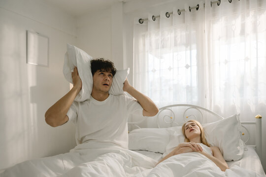 Couple lying in bed with woman snoring and man appearing annoyed, showing sleep disturbance, relationship frustration. real-life bedroom situation. snoring, couple, bed, sleep. woman. couple-problem.