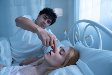 Annoyed man trying to stop his partner from snoring by pinching her nose while she sleeps, depicting sleep disturbance, relationship tension, snoring, couple, bed, sleep. woman. couple-problem.