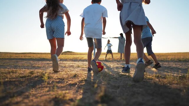 Play soccer at sunset child and kid run on field with parent and family silhouette ball on grass play continues under warm sun child kicking colorful ball on dry grass sun flare long shadow warm