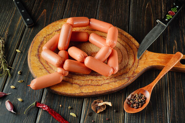 Fresh sausages are arranged in a circular pattern on a wooden cutting board. Nearby, a wooden spoon...