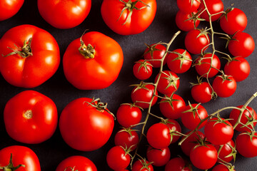 Top view of fresh ripe red tomatoes and cherry tomatoes arranged on a dark background. Vibrant organic vegetables for healthy eating, cooking, and vegetarian food concepts.