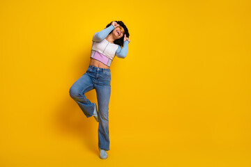 Happy young woman with curly hair in casual outfit dancing joyfully against bright yellow...