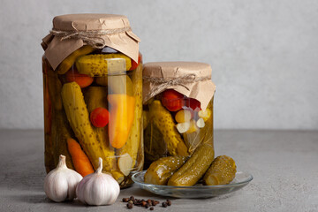 Glass jars filled with assorted pickled vegetables - cucumbers, peppers, carrots, and tomatoes. Garlic, peppercorns, and a dish of pickles.