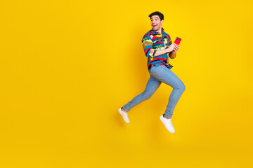 Young handsome male model in colorful shirt leaps with phone against yellow background showcasing fun lifestyle and fashion advertising vibe