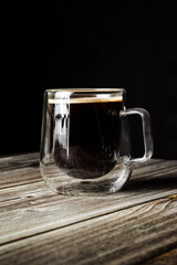 Black coffee in a clear glass cup on wooden surface, captured with dramatic contrast and sharp details.