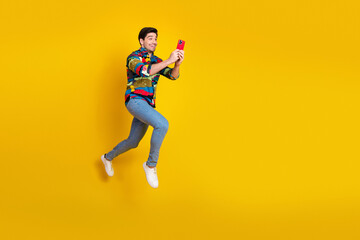Young man leaps in mid air selfie against bright yellow background wearing colorful shirt jeans and white sneakers
