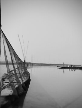 Vintage black and white photograph of a traditional sailing boat docked on a calm body of water with a distant vessel on the horizon