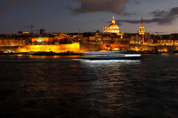Valletta, Malta at night with illuminated landmarks. A blurred tourist boat shot with long exposure...