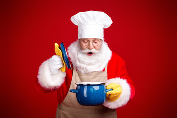 Santa the chef in a red holiday kitchen prepares a Christmas feast with a blue pot and plates while smiling and cooking