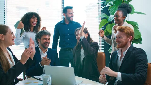 Happy business team celebrating success during meeting. Colleagues smiling and giving high fives around table. Excited coworkers enjoying achievement in office after productive collaboration.
