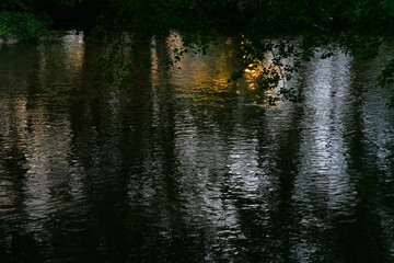 Mysterious atmosphere: reflection of trees and orange sunset in dark water