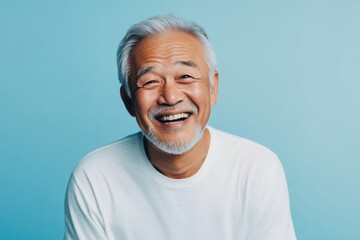 Obraz premium Happy senior Asian man smiling broadly, radiating cheerfulness and vitality against a vibrant blue background