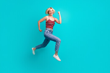 Young woman jumps with joy in a bright turquoise studio showing casual fashion lifestyle and fitness energy for a dynamic carefree and stylish advertising image